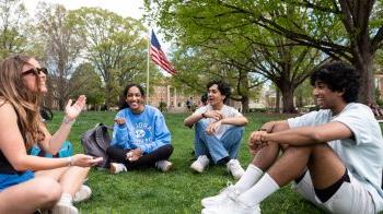 Four students talking and sitting on the lawn of McCorkle Place on the campus of UNC-Chapel Hill